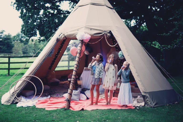Three children stood by a baby tipi decorated for a party with the tipi bank panel rolled up